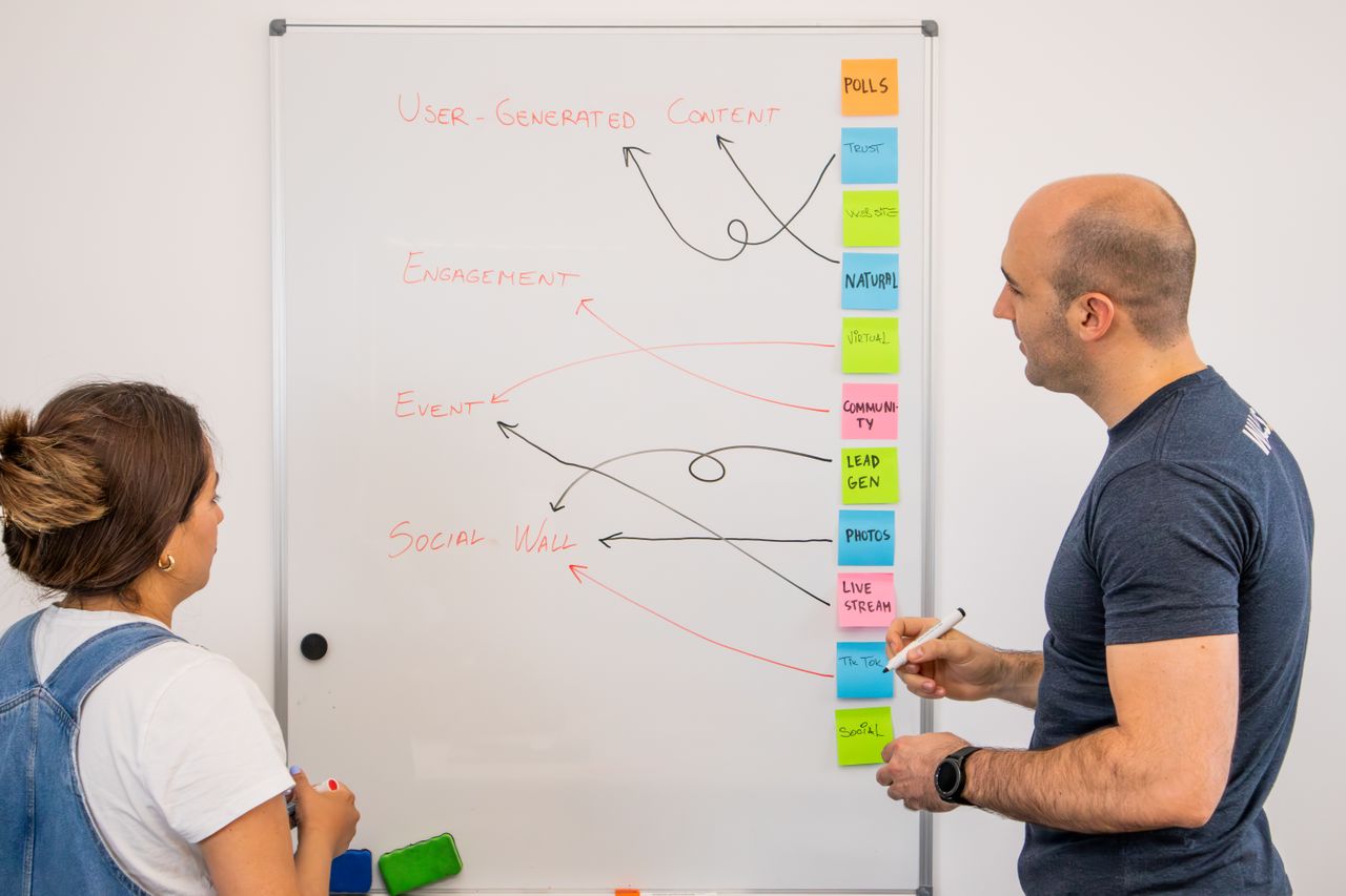 Two colleagues exchange ideas at a whiteboard during a creative strategy meeting.